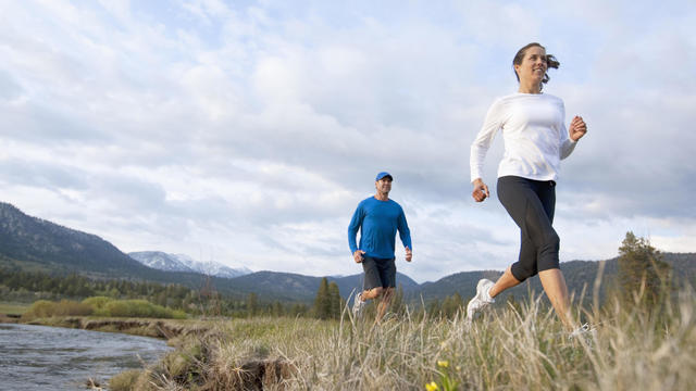 An athletic couple trail running through a field next to a river. 